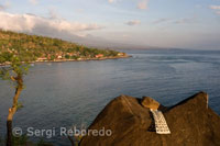 Una plegaria sobre una roca con vistas al pequeño pueblo pescador de Amed, con el fondo del monte Gunung Agung (3142m).  Este de Bali. 