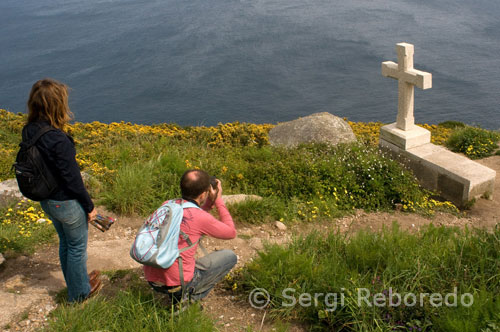 Algunos turistas fotografiado un cruceiro situado en la parte trasera del faro de Fisterra.