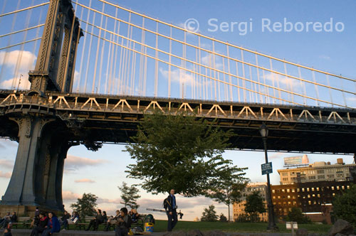 Un fotógrafo bajo el puente de Manhattan Bridge.  Este puente siempre ha vivido a la sombra de su ilustre hermano mayor, al sur. Inaugurado en 1909, este puente no tiene la gracia del Brooklyn (es una maraña de cables en azul y blanco, está revestido por una alambrada francamente carcelaria, el paseo peatonal está al costado sur, no en el centro, y hay que soportar ruidos y temblores del metro), pero tiene sus ventajas. Primera: su ubicación en pleno Chinatown. Después de una comida en New York Noodle Town (28 y medio Bowery), allí mismo, en la esquina de Bowery y Canal, están las escaleras que dan acceso al puente. En cuestión de minutos se disfrutan el maravilloso paisaje y la vista del Brooklyn Bridge.  Después de caminar una media hora, bajas otra serie de escaleras y en cinco minutos más estás en Down Under Manhattan Bridge Overpass (DUMBO). Hace una década, cuando los artistas se instalaron en sus antiguos galpones y fábricas, algunos decían que era demasiado siniestro allí debajo del puente Manhattan, y que nunca se podría crear un ambiente de barrio; pero allí está, con cada vez más gente guapa, galerías, restaurantes y tiendas. De diseño se destacan Prague Kolektiv (143 Front Street), meca de muebles checos del siglo XX; Baxter & Liebchen (33 Jay Street), con piezas danesas de Jacobsen, Henningsen y otros, y Wonk (68 Jay Street), mobiliario funcional e hipermoderno. En Loopy Mango Front (117 Front Street) te vestirán de vintage; en Pomme (81 Washington Street) pondrán a tus hijos a la última moda, y en Jacques Torres Chocolate (66 Water Street) encontrarás una razón para abandonar esa dieta neoyorquina de ensaladas y Coca- Cola light. Para comer están el brunch tranquilo en Dumbo General Store (en 111 Front Street); cocina fusión hindú-tailandesa en Rice (81 Washington), y comida americana clásica en Bubby's (1 Main), donde por la noche a veces tocan música. El puente de Manhattan es un puente colgante que cruza el East River en Nueva York , que conecta el Bajo Manhattan (en la calle Canal) con Brooklyn (en Flatbush Avenue Extension) en Long Island. It was the last of the three suspension bridges built across the lower East River, following the Brooklyn and the Williamsburg bridges. Fue el último de los tres puentes colgantes construidos en toda la parte baja del río del Este, tras la Brooklyn y el Williamsburg puentes. The bridge was opened to traffic on December 31, 1909 and was designed by Leon Moisseiff , [  1 ] who later designed the infamous original Tacoma Narrows Bridge that opened and collapsed in 1940. El puente se abrió al tráfico el 31 de diciembre de 1909 y fue diseñado por León Moisseiff , [1]  que más tarde se diseñó el famoso original Tacoma Narrows Bridge que se abría y se derrumbó en 1940. It has four vehicle lanes on the upper level (split between two roadways). Tiene cuatro carriles de vehículos en el nivel superior (divididos entre dos caminos). The lower level has three lanes, four subway tracks , a walkway and a bikeway . El nivel inferior tiene tres carriles, cuatro vías del tren , una pasarela y un carril para bicicletas .  The upper level, originally used for streetcars , has two lanes in each direction, and the lower level is one-way and has three lanes in peak direction. El nivel superior, utilizado inicialmente por los tranvías , tiene dos carriles en cada dirección, y el nivel inferior es de sentido único y tiene tres carriles en dirección máxima. It once carried New York State Route 27 and later was planned to carry Interstate 478 .  Llevó una vez en Nueva York la Ruta Estatal 27  y más tarde fue planeado para llevar a la Interestatal 478 .  No tolls are charged for motor vehicles to use the Manhattan Bridge.  N sujetas a peaje para vehículos de motor a utilizar el puente de Manhattan.