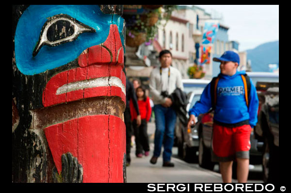 Tótem y turistas caminando en las calles de Juneau. Alaska, EE.UU.. La ciudad y el municipio de Juneau es la capital de Alaska. Es un municipio unificado situado en el canal inglés en el panhandle de Alaska, y es la segunda ciudad más grande de Estados Unidos por área. Juneau es la capital de Alaska desde 1906, cuando el gobierno de lo que era entonces el Distrito de Alaska fue trasladado de Sitka según lo dictado por el Congreso de Estados Unidos en 1900. El municipio unificado el 1 de julio de 1970, cuando la ciudad de Juneau se fusionó con la ciudad de Douglas y los alrededores Mayor Juneau Borough para formar el municipio la autonomía actual. El área de Juneau es más grande que la de Rhode Island y Delaware individualmente y es casi tan grande como los dos estados combinados. Downtown Juneau se encuentra en la base del Monte Juneau ya través del canal de la isla de Douglas. A partir del censo de 2010, la ciudad y el municipio tenía una población de 31.275. En julio de 2013, la estimación de la población de la Oficina del Censo de Estados Unidos era 32.660, por lo que es la segunda ciudad más poblada de Alaska después de Anchorage. (Fairbanks es sin embargo la segunda área metropolitana más grande en el estado, con más de 97.000 residentes.) Entre los meses de mayo y septiembre, la población diaria de Juneau pueden aumentar en aproximadamente 6.000 personas de visitar los buques de crucero.