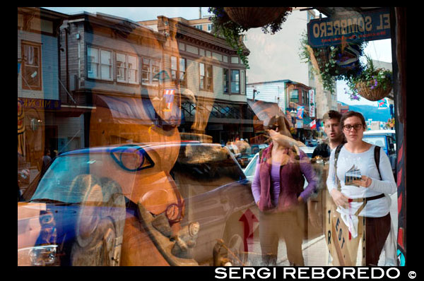 Las personas reflejadas en el escaparate de Tótem Shop, Juneau Alaska. Artesanías indígenas tienda, Juneau, Alaska. Indian Art Local y coleccionables. Tienda que ofrece el arte indígena local y objetos de colección. Título tomado de la etiqueta en la estera. Vista de grandes y pequeños tótems delante de tienda de curiosidades en Juneau, Alaska, con el reloj de la izquierda del gran tótem. Signos de edificio leen: "objetos curiosos visitantes son bienvenidos.". y "The Nugget Shop." ... Los coleccionistas de arte del fotógrafo encontrarán una fiesta para los ojos aquí. Impresionante paisaje natural de Juneau ha inspirado a muchos artistas cuyas pinturas, dibujos y las fotos se muestran en toda la ciudad. Escultura y tótems tallados son también piezas de arte popular. Tome un paseo por el centro - hay varias galerías agrupadas a lo largo de un par de cuadras de South Franklin Street - o en los distritos comerciales Mendenhall Valley para encontrar algo que se le antoje.