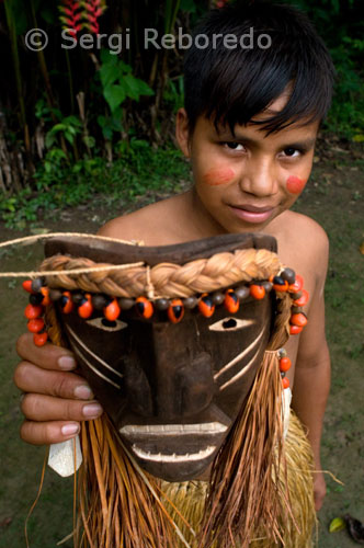 Poblat yagua. Un adolescent mostra una de les màscares que venen com artesania local. A més de les activitats tradicionals d'horticultura de frega i crema, caça, pesca i recollida, els Yaguas es troben involucrats en la comercialització de pells, fusta, carn i fruites silvestres, així com en la arròs i jute per a la venda en el mercat.