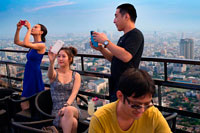 Bangkok. Asian people taking pictures. Banyan Tree Rooftop Vertigo & Moon Bar, Restaurant, , Bangkok , Thailand. View of the city, Vertigo Bar and Restaurant, roof of the Banyan Tree Hotel, at dusk Bangkok, Thailand, Asia. Reaching for the clouds at Vertigo and Moon Bar on the 61st floor of the Banyan Tree hotel is one of the best ways to end a long day in Bangkok. There is no lack of rooftop bars in town but Vertigo has always been amongst the favourites. With an unusual narrow and elongated shape, the entire top of the building is occupied by both the bar and the restaurant and gives the unusual impression of being aboard a spaceship in the sky. Located on Sathorn road, a very large busy avenue peppered with tall glass and metal skyscrapers and not far from the Lumpini park and Silom area, Banyan Tree is a name often associated with luxury. 