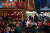 Bangkok. Bars, restaurants and nightlife in khao san road. Bangkok. Food stall. Bangkok. Khaosan Road or Khao San Road is a short street in central Bangkok, Thailand. It is in the Banglamphu area of (Phra Nakhon district) about 1 kilometre (0.62 mi) north of the Grand Palace and Wat Phra Kaew. "Khaosan" translates as "milled rice", a reminder that in former times the street was a major Bangkok rice market. In the last 20 years, however, Khaosan Road has developed into a world famous "backpacker ghetto". It offers cheap accommodation, ranging from "mattress in a box" style hotels to reasonably priced 3-star hotels. In an essay on the backpacker culture of Khaosan Road, Susan Orlean called it "the place to disappear". 