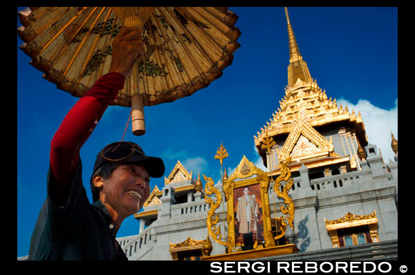 Umbrella seller. Facade of a temple, Wat Traimit, Bangkok, Thailand. Wat Traimit in Bangkok. Temple Of Golden Buddha In Chinatown. Located at the end of Chinatown's Yaowarat Road, near Hualampong Railway Station, Wat Traimit houses the world's largest massive gold seated Buddha measuring nearly five metres in height and weighing five and a half tons. In the past, artisans crafted the Buddhas in gold and disguised them from invading armies by a covering of stucco and plaster. The Buddha at Wat Traimit was discovered by accident when it was accidentally dropped as it was being moved, revealing, under a casing of plaster, a beautiful solid gold Sukhothai style Buddha. Pieces of the plaster are still kept on display.