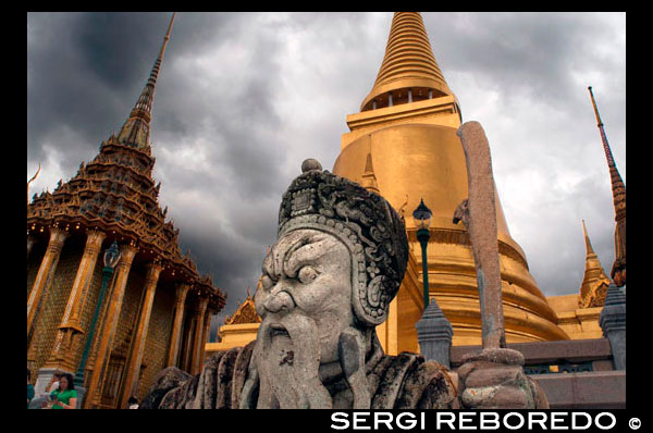 Stupa de oro y piedra Guardián Wat Phra Kaew, cerca del Gran Palacio Real de Bangkok Tailandia. Gigante Tutor en el frente de la estupa de oro Phra Sri Rattana Chedi y biblioteca Phra Mondop en Wat Phra Kaew, Bangkok, Tailandia. El Gran Palacio LBTR: Phra Borom Maha Ratcha Wang es un complejo de edificios en el centro de Bangkok, Tailandia. El palacio ha sido la residencia oficial de los Reyes de Siam (y más tarde Tailandia) desde 1782. El rey, su corte y su gobierno real se basaron en los terrenos del palacio hasta 1925. El actual monarca, el rey Bhumibol Adulyadej (Rama IX ), actualmente reside en Chitralada Palace, pero la Gran Palacio aún se utiliza para actos oficiales. Varias ceremonias reales y las funciones del Estado se llevan a cabo dentro de los muros del palacio cada año. El palacio es uno de los atractivos turísticos más populares en Tailandia. El Atrio o Khet Phra Racha Que Chan Na de la Grand Palace está situado al noroeste del palacio (el noreste siendo ocupado por el Templo del Buda Esmeralda). Entrando por la puerta principal Visetchaisri, el Templo del Buda Esmeralda se encuentra a la izquierda, con muchos edificios públicos ubicados a la derecha. El Templo del Buda de Esmeralda o Wat Phra Kaew formalmente conocido como Wat Phra Si Rattana Satsadaram, es una capilla real situada dentro de los muros del palacio. Refiere incorrectamente como un templo budista, es de hecho una capilla; que tiene todas las características de un templo a excepción de la zona de habitación para los monjes. Construido en 1783, el templo fue construido de acuerdo con la antigua tradición que se remonta a Sukotai, una capilla real dentro de los terrenos del palacio real en Sukhothai, y Wat Phra Sri Sanpetch en Ayutthaya. El famoso Buda de Esmeralda se mantiene dentro de los terrenos del templo.