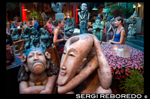 Sawasdee House Restaurant ram buttri bangkok. Soi Rambuttri. Bangkok. Thailand. Indonesian statues and figures.  Great cocktails and yummy Northern Thai food are served at this jungle restaurant. Try the house cocktail named after the place: a twist on a mojito with Thai-style liquor, lie back in your wicker chair surrounded by greenery and listen to the gentle hum of the street. Northern-style sausage and deep-fried dried pork make great beer snacks and the specials board is displayed on a vintage rickshaw outside. Whether you are alone, in a pair or even part of a group this bar and restaurant offers perfect respite from busy Rambuttri. Foreign tourists and backpackers drink and dine at night in an outdoor bar on Soi Rambuttri near Khao San Road, Bangkok. Part of Rambuttri runs parallel to Khao San, but despite being located so close by these two streets are different worlds. Rambuttri gives you a taste of how Bangkok used to look before all the skyscrapers arrived. Leafy banyan trees shade the pavements and the vibe sways more towards local than backpacker, despite a number of them now choosing to stay here rather than on the famous street itself. Rambuttri is Khao San's more attractive, well behaved brother. The entire horse-shoe-shaped road takes around 30 minutes to walk along. This street has a great mix of guesthouses, restaurants, bars and street food stalls. Most of the shops are similar to those you find anywhere in the area selling the usual T-shirts, DVDs and other tourist trinkets.