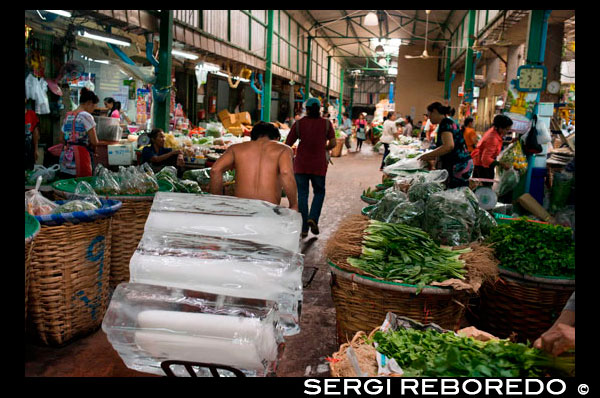 Venedor de gel. Els productes agrícoles com Mercat Central de Wang Burapha Phirom. Carrer Ban Mo. Bangkok. Àsia. Pak Khlong Talat (Mercat de les Flors). Bangkok. Pak Khlong Talat és un mercat a Bangkok coneguda per les seves flors a l'engròs. No obstant això, poc s'ha escrit sobre els volums de fruites i verdures fresques en el qual Pak Khlong Talat va ser una vegada establerta durant el seu regnat com el major mercat de productes a granel de Bangkok. Durant una visita primerenca matí de diumenge, vam explorar una de les més impressionants mostres de productes frescos en els quals m'he trobat. El Pak Khlong Talat és un mercat de productes a l'engròs, és evident per les seves exhibicions massives de fruites i verdures. No es teixeixen cistells la mida de barrils de vi que són la llar de gingebre ratllat, els xilis, i les taronges; manats d'herba de llimona i espàrrecs amb prou feines capaç d'encaixar sota el braç; camions de cols, cebes i all. El gran volum de producció és increïble! Hi ha una gran quantitat de moviment amb el producte en si. Cotxes de mà, apilats sis o vuit peus d'alt amb bosses i cistelles, es poden observar regularment el portaven pels carrers estrets. Aquests béns estan en camí per ser lliurat a altres mercats o restaurants. Enormes pantalles belles i agrestes, de fruites i hortalisses fresques s'estiren més i més en tot el mercat. Gairebé la fruita perfecta s'estableixen en la repetició de files per als compradors potencials. La varietat és interminable. Algunes pantalles no eren els de taula muntatges solem veure. El mercat sembla estendre des de cases-botiga de dos i tres pisos incrustats al llarg dels carrers estrets del mercat. Vestíbuls Garatge serveixen com a àrees per organitzar temporalment piles de productes frescos. El que fa que el mercat Pak Khlong Talat memorable i diferent d'altres mercats que hem visitat és la tranquil·litat tranquil que evoca. És bastant grans (diversos sou d'ample) i perquè està a Bangkok, esperava que s'omple de gent, tant els tailandesos i turistes estrangers.
