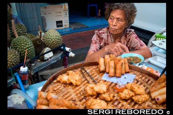 Mujer que vende rollos pring y frutas durian. Chinatown de Bangkok, Tailandia. Parada del mercado y la comida de la calle están preparando en el barrio chino de Bangkok, Tailandia. Yaowarat, el barrio chino de Bangkok, es el más famoso destino comida de la calle en el mundo y el distrito de comedor favorito local. En esta aventura la noche temprano, traemos a descubrir los sabores sofisticados de comunidad de 200 años de Bangkok que es rica en tradición entre Tailandia y China y la comida deliciosa. Durante el recorrido usted tendrá que caminar para explorar y degustar la cocina local de 7 restaurantes famosos, varió de vendedores ambulantes de alimentos a renombrados comensales entre Tailandia y China. Entre cada lugar de degustación, obtendrá la exposición detrás de la escena de este barrio único: el cumplimiento de los personajes animados del bazar comida, escuchar sus historias memorables, y visitar monumentos religiosos y culturales. Es nuestra meta para ofrecerle una deliciosa y única aventura que pondrá de relieve su viaje a Bangkok con la experiencia entusiasta más memorable. Siga la manada de lobos. Con un montón de cosas para ver y una gran variedad de alimentos para elegir, incluso los tailandeses de otras partes del país tuvo dificultades para navegar a sí mismos en Yaowarat. Nuestro tour de 3.5 horas tiene como objetivo ayudar a los visitantes dan a conocer el secreto de Chinatown a través de sus diversos gustos y fascinante tradición. Según lo recomendado por CNN Travel, nuestra Yawarat Noche Foodie Walk es sólo un camino perfecto para aquellos que buscan experimentar calles de visita obligada de Bangkok como ya se ha visto en numerosos shows de viaje y películas de gran hit, incluyendo Hangover Part 