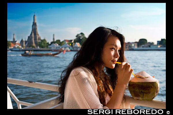 Bona noia romàntica en un vaixell prop de Temple Wat Arun i del riu Chao Praya. Beure 1 coconout. Chao Phraya vaixell turístic. El BTS Skytrain es dóna la mà amb el proveïdor de Bangkok major públic d'aigua de transport, el Chao Phraya Vaixell exprés Co, Ltd (Establert fa 38 anys) per introduir un nou servei de transport d'aigua "El Chao Phraya vaixell turístic ". Aquest servei ofereix als turistes l'oportunitat de veure Bangkok des d'una perspectiva totalment nova, en un sol dia, el turista pot viatjar fàcilment en els vaixells d'alta quantitat de moll a moll sense preocupar-se per la compra de bitllets de vaixell o perdre. A més, poden visitar molts llocs turístics atractius com ara el temple de l'alba, i el gran Buda reclinat en Wat Pho. Viatge al llarg del riu Chao Phraya. El riu Chao Phraya juga molts papers en la vida tailandesa, de fet, és considerada com l'artèria principal de la nació. Gran part de la història tailandesa es pot rastrejar al llarg de les bandes del riu Chao Phraya. A mesura que flueix, el riu porta amb si la història i la cultura del país. El servei Chao Phraya Vaixell Turístic et porta a 8 molls diferents que donen accés a les atraccions més famoses de Bangkok moltes de les quals estan en el Casc Històric Rattanakosin Island, que es va instal·lar durant les eres Thonburi i Rattanakosin. Antics temples, palaus i comunitats al llarg de les ribes del riu Chao Phraya, ens diuen que el riu Chao Phraya ha proporcionat suport de la gent i ha donat lloc al naixement d'una civilització.