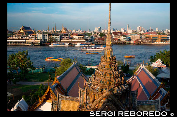 Paisatge en la posta de sol del riu Chao Praya del temple de Wat Arun. Bangkok. Tailàndia. Àsia. Wat Arun, conegut localment com Wat Chaeng, està situat a la riba oest (Thonburi) del riu Chao Phraya. És fàcilment un dels més impressionants temples a Bangkok, no només a causa de la seva ubicació al costat del riu, sinó també perquè el disseny és molt diferent als altres temples que es poden visitar a Bangkok. Wat Arun (o temple de l'alba) és en part formades per torres decorades amb vius colors i s'alça majestuosa sobre l'aigua. Wat Arun és gairebé directament davant de Wat Pho, així que és molt fàcil arribar a. Des Sapphan Taksin embarcador es pot agafar un vaixell pel riu que s'atura al moll 8. Des d'aquí un petit vaixell de transport que et porta d'un costat del riu a l'altre per només 3 baht. L'entrada al temple és de 100 Baht. El temple està obert dies de 08:30 a 17:30. El recomanem passar almenys una hora de visitar el temple. Encara que és conegut com el Temple de l'Aurora, és absolutament impressionant al vespre, sobretot quan s'il·lumina a la nit. El moment més tranquil per visitar, però, és d'hora al matí, abans de les multituds. Donada la bellesa de l'arquitectura i l'artesania fina, no és sorprenent que Wat Arun és considerat per molts com un dels temples més bonics de Tailàndia. L'agulla (Prang) a la vora del riu Chao Phraya és un de Bangkok llocs d'interès turístic. Compta amb una torre imponent de més de 70 metres d'altura, molt ben decorat amb petits trossos de vidre acolorit i porcellana xinesa col·locats delicadament en patrons intricats.