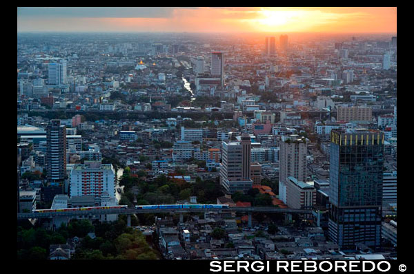 Posta de sol Paisatge de Xarxa Sky Restaurant terrat. Bangkok. Tailàndia. A la planta superior de l'Centara Grand gratacels al centre de la ciutat. La vista Chinatown, més el Gran Palau i temples de l'illa de Rattanakosin. Xarxa Sky és un dels nous bars del terrat i restaurant a Bangkok. Si bé no ofereix colpejar la riba del riu o vistes copes dels arbres que altres bars del terrat gaudeixen, té bastant impressionants vistes panoràmiques de 360 ???? graus del seu pis 55, un dels llocs més convenients de la ciutat. Si vostè visita Bangkok, és probable que el resultat final serà anar de compres a la zona de Siam, on es troben els més grans i moderns centres comercials, com el llegendari Siam Paragon, MBK i el CentralWorld recentment reconstruït. Xarxa Sky bar és part del Centara Grand Hotel, que en si és en realitat part d'aquest gegantesc centre comercial Central World. Pel que sembla ser una combinació perfecta: botiga fins als seus gotes de targetes de crèdit, després de recuperar-se de quilòmetres i quilòmetres de caminar amb un sopar o una copa de vi amb vistes inoblidables del terrat per sobre del propi centre comercial.