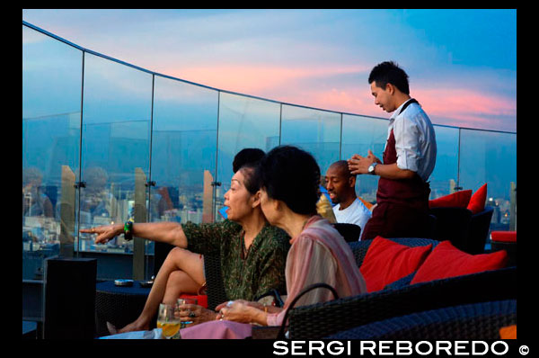 Xarxa Sky Bar al terrat. Bangkok. Tailàndia. A la planta superior de l'Centara Grand gratacels al centre de la ciutat. La vista Chinatown, més el Gran Palau i temples de l'illa de Rattanakosin. Xarxa Sky és un dels nous bars del terrat i restaurant a Bangkok. Si bé no ofereix colpejar la riba del riu o vistes copes dels arbres que altres bars del terrat gaudeixen, té bastant impressionants vistes panoràmiques de 360 ???? graus del seu pis 55, un dels llocs més convenients de la ciutat. Si vostè visita Bangkok, és probable que el resultat final serà anar de compres a la zona de Siam, on es troben els més grans i moderns centres comercials, com el llegendari Siam Paragon, MBK i el CentralWorld recentment reconstruït. Xarxa Sky bar és part del Centara Grand Hotel, que en si és en realitat part d'aquest gegantesc centre comercial Central World. Pel que sembla ser una combinació perfecta: botiga fins als seus gotes de targetes de crèdit, després de recuperar-se de quilòmetres i quilòmetres de caminar amb un sopar o una copa de vi amb vistes inoblidables del terrat per sobre del propi centre comercial.