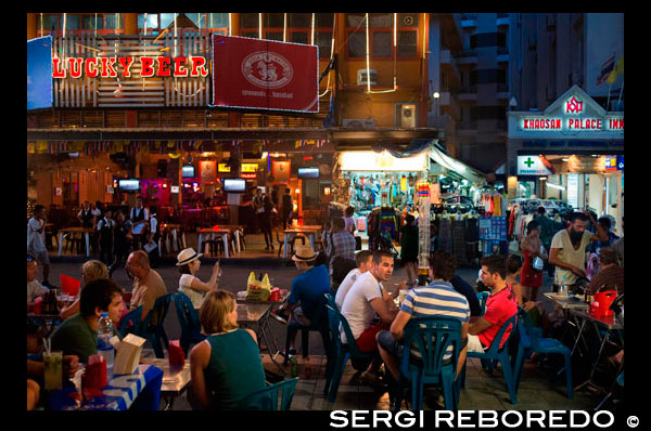 Bars, restaurants and nightlife in khao san road. Bangkok. Food stall. Bangkok. Khaosan Road or Khao San Road is a short street in central Bangkok, Thailand. It is in the Banglamphu area of (Phra Nakhon district) about 1 kilometre (0.62 mi) north of the Grand Palace and Wat Phra Kaew. "Khaosan" translates as "milled rice", a reminder that in former times the street was a major Bangkok rice market. In the last 20 years, however, Khaosan Road has developed into a world famous "backpacker ghetto". It offers cheap accommodation, ranging from "mattress in a box" style hotels to reasonably priced 3-star hotels. In an essay on the backpacker culture of Khaosan Road, Susan Orlean called it "the place to disappear".  It is also a base of travel: coaches leave daily for all major tourist destinations in Thailand, from Chiang Mai in the north to Ko Pha Ngan in the south, and there are many relatively inexpensive travel agents who can arrange visas and transportation to the neighbouring countries of Cambodia, Laos, Malaysia, and Vietnam. Khaosan shops sell handcrafts, paintings, clothes, local fruits, pirated CDs, DVDs, a wide range of fake IDs, used books, plus many useful backpacker items. During late evening, the streets turn into bars and music is played, food hawkers sell barbecued insects, exotic snacks for tourists, and there are also locals flogging ping pong shows. There are several pubs and bars where backpackers meet to discuss their travels. The area is internationally known as a center of dancing, partying, and just prior to the traditional Thai New Year (Songkran festival) of 13-15 April, water splashing that usually turns into a huge water fight. One Thai writer has described Khaosan as "...a short road that has the longest dream in the world".[2] A Buddhist temple under royal patronage, the centuries-old Wat Chana Songkram, is directly opposite Khaosan Road to the west, while the area to the northwest contains an Islamic community and several small mosques.