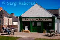 Ulster Folk & museo del transporte. Ballycultra edificios de la ciudad. Ballycultra un salón de té. Tés Almuerzos de café. Estas cuatro casas fueron construidas en la década de 1870 como la ciudad de Dromore ampliado. En 1903, la casa más grande en el extremo de la terraza, con dos habitaciones en planta baja, estaba ocupada por un zapatero, José Robert Magill. Su negocio de reparación de calzado se llevó a cabo en la sala y Robert, su esposa y sus seis hijos ocuparon el cuarto del fondo y las habitaciones de arriba. El emprendedor Sr. Magill adquirió la casa de al lado, en 1913 y estableció un negocio de reparación de bicicletas pequeñas. Las casas eran originalmente parte de una terraza grande en la calle que llevó a Dromore Presbiteriana de casa de reunión, o la iglesia. Las otras casas en la terraza son más pequeños, con una sala de planta baja, individual y una habitación de arriba y su distribución de la sala es una reminiscencia de las casas tradicionales en el campo de los alrededores. Aunque las casas eran pequeñas, los ocupantes entre 1901 y 1911 fueron todas las familias individuales, cada uno de los cuatro o cinco personas. Muchos de los habitantes de la calle trabajó en las fábricas de ropa locales. El taller de carpintería en el extremo de la terraza es típico de las empresas de artesanía local, que atiende a las necesidades de una ciudad pequeña. Ubicación original: Meeting Street, Dromore, Condado de Down