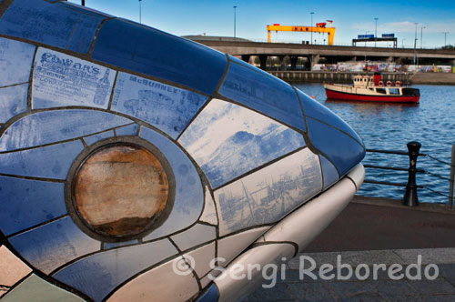 The big fish sculpture is located in Belfast since 1999, at the Donegall Quay.It was commissioned by the laganside corporation to celebrate the regeneration of the river lagan in Belfast.It is postioned at a place were the farset and lagan rivers join (an important location in the history of Belfast. Some interesting facts about this sculpture. It is 10m long. The outer layer is constructed of printed ceramic tiles.These tiles are printed with details of Belfast's history from the 1600s to the present day. The artists' name who created the sculpture was a local man called John Kindness. A time capsule with information about Belfast is placed inside for future generations to discover! It is a popular spot for tourist photographs, so visit it when you come to Belfast so you can say "I was there". It is just a 10 minute stroll from the city centre and close to the Belfast Odyssey Entertainment Centre and the lagan weir.