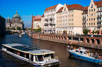 Berlin. Germany. A tourist boat on the Spree river alongside The Nikolaiviertel or St. Nicholas Quarter on a sunny day. Nicholas quarter with the berliner dom or cathedral in the background on a sunny day. The area contained some of the oldest building. The area got its name from the parish church in its centre, dating back to the 13th century. This district is just about the only part of Berlin that has a medieval look to it, with small gabled houses and narrow alleyways. Once the home of artists and writers, the Nicolaiviertel is nowadays filled with tourists visiting the souvenir shops and popular restaurants.