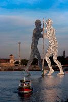 Berlín. Alemanya. Escultura metàl · lica anomenada Home Molècula per Jonathan Borofsky al riu Spree de Berlín. Home Molècula és una sèrie d'escultures d'alumini, dissenyats per l'artista nord-americà Jonathan Borofsky, instal · lades en diversos llocs del món, incloent Berlín, Alemanya, i Council Bluffs, Iowa, EUA. Les primeres escultures Home de la molècula es van realitzar el 1977 i 1978 a Los Angeles, EUA. Les escultures es componen de tres éssers humans que s'inclinen l'un cap a l'altre, els cossos dels quals estan plens de centenars de forats, els forats de representant de "les molècules de tots els éssers humans que s'uneixen per crear la nostra existència". Una escultura relacionat és l'home del martell
