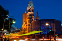 Germany, Berlin, Kaiser Wilhelm memorial Church at twilight. The Protestant Kaiser Wilhelm Memorial Church (in German: Kaiser-Wilhelm-Gedächtniskirche, but mostly just known as Gedächtniskirche [???d?çtn?s?k??ç?]) is located in Berlin on the Kurfürstendamm in the centre of the Breitscheidplatz. The original church on the site was built in the 1890s. It was badly damaged in a bombing raid in 1943. The present building, which consists of a church with an attached foyer and a separate belfry with an attached chapel, was built between 1959 and 1963. The damaged spire of the old church has been retained and its ground floor has been made into a memorial hall. The Memorial Church today is a famous landmark of western Berlin. Inside the church, opposite the entrance, is a figure of Christ which is suspended above the altar. This is made from tombak and was designed by Karl Hemmeter. The cross on the altar, by Peter Tauchnitz, is of gilt silver with 37 rock crystals. 