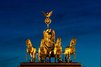 Cuadriga en la puerta de Brandenburgo en la noche, Berlín, Alemania. La Puerta de Brandenburgo (alemán: Brandenburger Tor) es una antigua puerta de la ciudad, reconstruida en el siglo 18 como un arco de triunfo neoclásico, y ahora uno de los hitos más conocidos de Alemania. Se encuentra en la parte occidental del centro de la ciudad de Berlín, en el cruce de la avenida Unter den Linden y Ebertstraße, inmediatamente al oeste de la Pariser Platz. A una cuadra hacia el norte se encuentra el edificio del Reichstag. La puerta es la entrada monumental de la avenida Unter den Linden, el famoso bulevar de tilos, que anteriormente condujo directamente a la ciudad palacio de los reyes de Prusia.