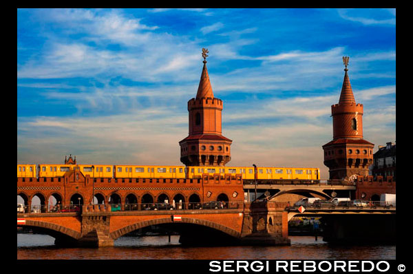 Alemanya, Berlín , el pont Oberbaumbrücke que uneix els districtes de Kreuzberg i Friedrichshain sobre el riu Spree . El Pont Oberbaum (alemany : Oberbaumbrücke ) és un pont de dos pisos de creuar el riu Spree de Berlín , considerada una de les ciutats llocs d'interès . Vincula Friedrichshain i Kreuzberg , els antics comtats que van ser dividits pel mur de Berlín , i s'ha convertit en un important símbol de la unitat de Berlín . El pis inferior del pont porta una carretera , que connecta Oberbaum Straße cap al sud del riu amb Warschauer Straße cap al nord . La coberta superior del pont porta Berlin línia U1 O- Bahn , entre Schlesisches Tor i estacions de Warschauer Straße . El pont apareix prominentment en la pel · lícula Run Lola Run 1998 . El pont està construït sobre l'antic límit del terme municipal amb el seu entorn rural , on una paret especial , construït al 1732 Un pont llevadís de fusta va ser construït com a part de la paret . ; va servir com a porta d'entrada a la ciutat . El nom es deriva de Oberbaumbrücke del tronc de l'arbre pesat , cobert de punxes de metall , que s'utilitza com un boom per bloquejar el riu a la nit per evitar el contraban . ( Baum significa arbre o biga de fusta en alemany , de manera que el nom significa alguna cosa així com " Upper [ Upstream ] Pont d'arbre" , no hi havia cap barrera tronc d'arbre a l'extrem occidental dels límits actuals de la ciutat , prop de l'actual Unterbaumstraße ( literalment en anglès : . Inferior [ Downstream ] arbre del carrer )