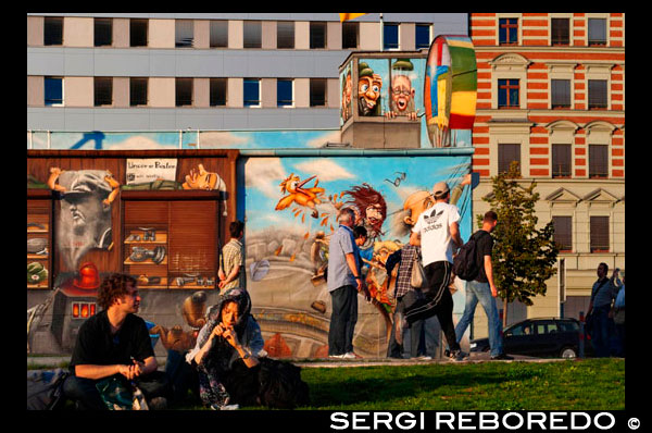 Germany, Berlin. A relaxing afternoon on the lawn of the East side gallery along the Spree. The East Side Gallery is an international memorial for freedom. It is a 1.3 km long section of the Berlin Wall located near the centre of Berlin on Mühlenstraße in Friedrichshain-Kreuzberg. The actual border at this point was the river Spree. The gallery is located on the so-called "hinterland mauer", which closed the border to East Berlin. The Gallery consists of 105 paintings by artists from all over the world, painted in 1990 on the east side of the Berlin Wall. The East Side Gallery was founded following the successful merger of the two German artists' associations VBK and BBK. The founding members were the speche of the Federal Association of Artists BBK Bodo Sperling, Barbara Greul Aschanta, Jörg Kubitzki and David Monti. It is possibly the largest and longest-lasting open air gallery in the world. Paintings from Jürgen Grosse alias INDIANO, Dimitri Vrubel, Siegfrid Santoni, Bodo Sperling, Kasra Alavi, Kani Alavi, Jim Avignon, Thierry Noir, Ingeborg Blumenthal, Ignasi Blanch i Gisbert, Kim Prisu, Hervé Morlay VR and others have followed. The paintings at the East Side Gallery document a time of change and express the euphoria and great hopes for a better, more free future for all people of the world. In July 2006, to facilitate access to the River Spree from O2 World, a 40 meter section was moved somewhat west, parallel to the original position A 23 meter section is scheduled to be removed on March 1, 2013, to make way for luxury apartments. None of the artists whose work will be destroyed were informed of these plans. The demolition work actually started on March 1, 2013. According to German news FOCUS, authorities were not aware of the start of the demolition. Due to the involvement of protesters, demolition was postponed until at least March 18, 2013.