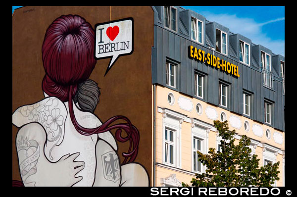 I love Berlin. East Side Hotel in front of East Side Gallery. The East Side Gallery is a 1.3 km-long painted stretch of the former Berlin Wall along the Mühlenstrasse in former East Berlin. It is the largest open-air gallery in the world with over one hundred original mural paintings. Galvanised by the extraordinary events which were changing the world, artists from all around the globe rushed to Berlin after the fall of the Wall, leaving a visual testimony of the joy and spirit of liberation which erupted at the time.   Wall murals had previously been a highlight for visitors and a Berlin attraction for years but were only to be found on the western side of the Wall. The artists transformed the grey concrete rearticulating this into a lasting expression of freedom and reconciliation.  Some of the best known paintings such as “The Mortal Kiss” by Dimitrji Vrubel, of Erich Honecker and Leonid Brezhnev’s mouth-to-mouth embrace and Birgit Kinder’s Trabi (Trabant) knocking down the Wall. They have provided popular postcard material until today. The paintings which still reflect the patchwork, eclectic and bohemian atmosphere of Berlin today are a mixed-bag of surreal images, political statements and graffiti-like effusions stretching from the Oberbaum Brücke to the Ostbahnhof.