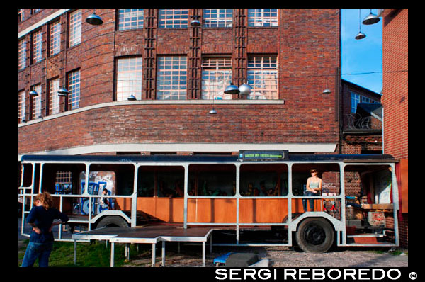 Berlin, Germany, on a old bus in Arena Berlin. Oversized benches and cars covered in grass at Arena Berlin. Cultural events in a listed factory building along the former GDR border. Today, this 7,000 sqm venue at the edge of the Spree River is the site for countless concerts, fairs and parties – but the building complex in Berlin’s Treptow district was originally used quite differently: Designed by architect Franz Ahrens, the arena was built in 1927 as a bus hall for Berlin's public transport system. At the time, it was Europe's largest free-standing hall and could hold 240 buses. During the Nazi period, it was turned into a weapons arsenal. After the Berlin Wall was built in 1961, it was no longer accessible due to its location; after the German reunification, Berlin’s public transport services officially closed the building altogether.  Various locations on one area  In the mid-1990ies, extensive refurbishments were carried out on the complex, and the Arena Berlin is now one of the most important venues for cultural events in the city. The Arena has been expanded over the years to include additional venues in the vicinity. The ‘Glass House’ of the Arena, a club, theatre and café, for example, is located in what was once a turner’s shop, offering panoramic views of the Spree River with its fully glazed façade.  Great views can also be enjoyed from aboard the club and restaurant ship MS Hoppetosse, which is anchored along the banks of the Spree River. The ship also hosts a reggae party every Sunday, entitled ‘Yaam’. The neighbouring ship features a swimming pool in the summer with plenty of space to lay in the sun, and changes into a roofed sauna landscape in winter.  Other venues of the Arena Berlin include the Arena Club, the restaurant ‘Anhalt’ and the bar ‘Freischwimmer’. The summer months are a busy time here, with concerts, parties, various annual events, like the European music festival ‘Popdeurope’, and open-air ‘Unplugged’ 