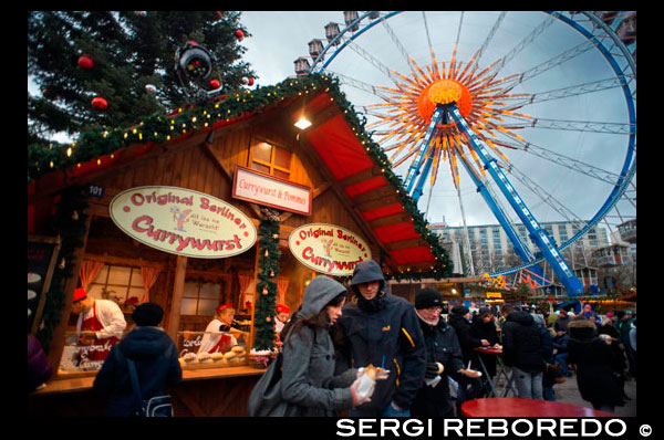 Roda de la fortuna i Currywurst en el mercat de Nadal davant de la font Neptunbrunnen , Alexanderplatz , Berlín . Snack- bar a Alexanderplatz . Les campanes , garlandes , nadales , arbres decorats ... Nadal ha arribat definitivament . Aquest moment especial de l'any , comença a fer-se sentir en tots els racons de la capital . No hi ha moltes ciutats al món que saben com donar la benvinguda al Nadal com Berlín . És un fet ben conegut que el poble alemany encanta celebrar el Nadal . Berlín no vol ser eclipsat per ciutats com Munic o Dresden , que són més àmpliament coneguts per les seves celebracions de Nadal . Compta amb mercats de Nadal seixanta repartides per tota la ciutat : tradicional o alternativa , especialitzada en artesanies o aliments , gratuït o de pagament , hi ha un mercat per a tots els gustos . Un dels mercats més turístiques i comercials , però al mateix temps un dels més característics , es porta a terme en els voltants de la plaça Alexanderplatz . Entrant per la Karl - Liebknecht - Strasse , al llarg de la plaça i acabant per Alexa , es troba un dels millors Weihnachtsmarkt la ciutat té per oferir. Un cop passat la porta principal brillant comencem a sentir el veritable esperit del Nadal . La cançó " Bon Nadal a tots " i altres clàssics es poden sentir just al costat de l'estàtua Neptunbrunnen , que al seu torn està envoltat per una de les moltes pistes de patinatge sobre gel que adornaran la ciutat aquest mes . Des del cel , el timó de transbordador de 50 metres mira cap amunt. Aquells que desafien les altures podran gaudir de belles vistes de tot el mercat i també el districte Mitte dels voltants . Hi ha carrerons llargs en ??què les cabines estan col · locats en files , les petites cases de fusta , sostres amb neu artificial , música , campanes , trineus i llums per tot arreu . És sens dubte una de les meravelles de l'hivern.