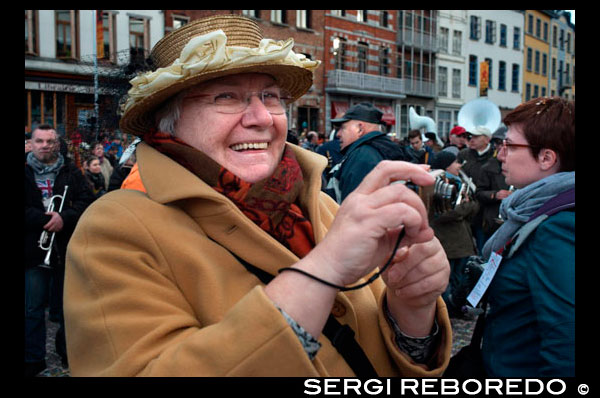 Older woman taking pictures. Music, dance, party and costumes in Binche Carnival. Ancient and representative cultural event of Wallonia, Belgium. The carnival of Binche is an event that takes place each year in the Belgian town of Binche during the Sunday, Monday, and Tuesday preceding Ash Wednesday. The carnival is the best known of several that take place in Belgium at the same time and has been proclaimed as a Masterpiece of the Oral and Intangible Heritage of Humanity listed by UNESCO. Its history dates back to approximately the 14th century. Events related to the carnival begin up to seven weeks prior to the primary celebrations. Street performances and public displays traditionally occur on the Sundays approaching Ash Wednesday, consisting of prescribed musical acts, dancing, and marching. Large numbers of Binche's inhabitants spend the Sunday directly prior to Ash Wednesday in costume. The centrepiece of the carnival's proceedings are clown-like performers known as Gilles. Appearing, for the most part, on Shrove Tuesday, the Gilles are characterised by their vibrant dress, wax masks and wooden footwear. They number up to 1,000 at any given time, range in age from 3 to 60 years old, and are customarily male. The honour of being a Gille at the carnival is something that is aspired to by local men