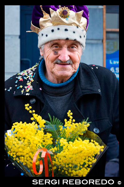 Binche, Hainaut, Belgium - Stand selling flowers during carnival parade in the streets on Mardi Gras. Belgium, carnaval of Binche. UNESCO World Heritage Parade Festival. Belgium, Walloon Municipality, province of Hainaut, village of Binche. The carnival of Binche is an event that takes place each year in the Belgian town of Binche during the Sunday, Monday, and Tuesday preceding Ash Wednesday. The carnival is the best known of several that take place in Belgium at the same time and has been proclaimed as a Masterpiece of the Oral and Intangible Heritage of Humanity listed by UNESCO. Its history dates back to approximately the 14th century. Events related to the carnival begin up to seven weeks prior to the primary celebrations. Street performances and public displays traditionally occur on the Sundays approaching Ash Wednesday, consisting of prescribed musical acts, dancing, and marching. Large numbers of Binche's inhabitants spend the Sunday directly prior to Ash Wednesday in costume. The centrepiece of the carnival's proceedings are clown-like performers known as Gilles. Appearing, for the most part, on Shrove Tuesday, the Gilles are characterised by their vibrant dress, wax masks and wooden footwear. They number up to 1,000 at any given time, range in age from 3 to 60 years old, and are customarily male. The honour of being a Gille at the carnival is something that is aspired to by local men