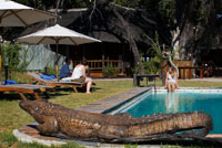 Exteriores del campamento Eagle Island Camp de Orient Express, en las afueras de la Reserva de Animales de Moremi, en Botswana. Situado en el Delta Central de Okavango, Eagle Island Camp es un campamento construido sobre el agua, con tiendas y tejados de paja, en una de las islas de la Laguna Xaxaba. Xaxaba significa literalmente “isla de árboles altos”. El campamento es un agradable refugio protegido del sol africano, gracias a la sombra proporcionada por una bóveda de árboles autóctonos. Se encuentra en uno de los lugares más vírgenes y naturales del delta, una región con gran variedad de canales y amplios humedales. La vida animal y de aves de esta región es muy abundante, pudiendo observarse a las especies a bordo de mekoros (piraguas tradicionales), barcas motorizadas, cruceros de 14 asientos al atardecer y un helicóptero Bell Jet Ranger (con coste adicional). Para los exploradores más intrépidos y con ansias de seguir rastros y ruidos en los arbustos, el campamento pone a su disposición paseos guiados. Además, las magníficas puestas de sol pueden disfrutarse -a cubierto de las lluvias- desde el Fish Eagle Bar o desde la plataforma elevada con vistas a la laguna. Eagle Island Camp ofrece actividades matutinas y al atardecer para avistar animales. Pueden hacerse en barcas motoras o en sigilosos mekoros (piraguas tradicionales) a través de las aguas claras del Okavango. 