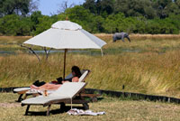 Una turista descansa plàcidament prenent el sol al campament Khwai River Lodge d'Orient Express a Botswana, a l'interior de la Reserva Salvatge de Caça Moremi, amb un elefant de fons. Un altre llocs en Moremi són: Les Salines de Makgadikagadi. Aquestes salines són famoses a Botswana i són les més grans en el món sencer. Aquests només han estat capaços d'atraure molts turistes que realment volen saber com es fa la sal. Molt abans, les cassoles es reconeix haver estat un llac enorme, però més tard split.Some dels llocs que veure a les cassoles Makagadikgadi són les migracions de flamencs al Santuari de Aus Nata, juntament amb la migració anual de zebres. Se li sorprendran en el paisatge del país. Xakanaxa Llacuna. Amb una ubicació estratègica al centre de reserva de Moremi, que és una llar als antílops boniques, així com els gossos salvatges. Les llacunes ofereixen el millor ambient que li farà seure i relaxar-se mentre gaudeix de la natura. Mashatu Game Reserve. Està reconegut com un dels vedats de caça amb més encant de la part meridional d'Àfrica i de propietat privada. Es troba situat a la part oriental de Botswana. Visitar aquesta reserva li donarà l'oportunitat de veure les rares espècies d'aus, per exemple marcials i negre àguila, calau, juntament amb els blauets i els rodets. Que es va a fer una ullada més de prop a aquestes espècies a la reserva de caça. Viatges de la nit també s'ofereixen a la reserva, això només s'organitzen per als turistes que volen veure els animals nocturns per exemple llops de terra, genetes, lleopards i molts altres. Fora del ciclisme de carretera, així com de conducció també és part del paquet.