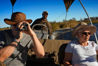 Una parella de turistes gaudeix d'un safari en barca des del campament Eagle Island Camp d'Orient Express , als afores de la Reserva d'Animals de Moremi , a Botswana . Moremi Crossing es troba a la zona més meridional de Chief s Island , en una petita illa plena de palmeres i diferents arbres , anomenada Ntswi . Aquesta illa està envoltada per les riques planes al · luvials de Moremi . L'accés es realitza en avioneta , després d'un curt vol escènic des Maun d'uns 20 minuts de durada . Durant aquest vol panoràmic sobre el fascinant Delta de l' Okavango , podrà gaudir dels apassionants dibuixos que creen els serpentejants canals d'aigua i els contrastos de colors amb les zones de terra ferma que s'eleven sobre les aigües del Delta . A la zona nord del Delta les aigües Okavango flueixen de forma ràpida i la vista es veu limitada per les altes canyes i papirs que creixen en el límit dels canals. A la zona del sud del Delta , als voltants de Moremi CROSSING , es gaudeix d'àmplies vistes de les planes al · luvials de la reserva de Moremi