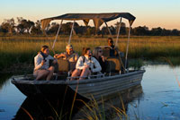 Los turistas disfrutas de los últimos rayos de sol en el safari acuático efectuado desde el campamento Eagle Island Camp de Orient Express, en las afueras de la Reserva de Animales de Moremi, en Botswana. El río Okavango nace en Angola y después de recorrer casi 1000 kms se divide en infinidad de riachuelos, canales y lagunas formando el área llamada Delta del Okavango (ya en Botswana). 15.000 kilómetros cuadrados ocupa este increible regalo de la naturaleza llena de aves de todos los colores, hipopótamos, cocodrilos, impalas, cebras, elefantes, búfalos, jabalíes... así como nenúfares, papiros y de la más variada fauna.  Los safaris se hacen tanto a pie como en lancha.  También se visitan aldeas dónde contemplar la vida humilde de sus habitantes : casas de madera compartiendo un surtidor de agua y sin luz. Además del moroko dónde llevar a los turistas, sus fuentes de ingreso son pequeños huertos, la pesca  y trabajos de artesanía.  RECOMENDACIONES Si lo que te interesa ver son grandes mamíferos, la mejor época para visitar el delta es de mayo a octubre, cuando las aguas están en niveles bajos. Si prefieres una vegetación verde y rabiosa cubierta de aves, la mejor época es la de las lluvias, de noviembre a abril. Los alojamientos situados en el corazón del delta son privados y son muy caros. La alternativa son los campamentos y los lodges del gobierno que se encuentran en la península de Moremi.  