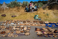 Improvisado mercadillo de artesanía a la llegada de los turistas en el campamento Batawana. En las inmediaciones del campamento Eagle Island Camp de Orient Express, en las afueras de la Reserva de Animales de Moremi, en Botswana hay un campamento donde residen un centenar de indígenas de la tribu Batawana. Es posible realizar excursiones en canoa para visitar su poblado.  La Artesanía de la terracota en el Distrito de Kgatleng de Botsuana fue declarada Patrimonio cultural inmaterial de la Humanidad en 2012 por la UNESCO.1 Se trata de la artesanía creada por las mujeres de la comunidad bakgatla ba kgafela del Distrito de Kgatleng, en el sudeste del país. Se utiliza tierra arcillosa, arenisca erosionada, óxido de hierro, boñiga de vaga, agua, hierba y madera para fabricar recipientes en los que se plasman motivos de rituales y creencias ancestrales de la comunidad. La recolección de la tierra se hace a través de la meditación de la maestra artesana. Una vez recolectadas la arcilla y la arenisca, se machacan y se criban. Tras ello se forma la pasta para modelar. Tras decorarse, se cuecen en un horno de pozo. La tradición se va trasmitiendo de generación en generación pero actualmente este arte corre peligro de desaparición debido a la disminución del número de maestras artesanas, los bajos precios de los productos acabados y el uso, cada vez más, de recipientes de producción de masa. Es por ello que la UNESCO lo incluyó en la Lista del Patrimonio Cultural Inmaterial que requiere medidas urgentes de salvaguardia.