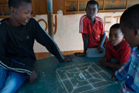 Unos niños juegan con chapas en un poblado cercano al campamento Khwai River Lodge de Orient Express en Botswana, en el interior de la Reserva Salvaje de Caza Moremi. Botswana. El patrimonio artístico más importante de Botsuana descansa en el legado de los bosquimanos, una tribu milenaria que supo plasmar, en las paredes de cuevas y rocas, su profunda espiritualidad. El arte rupestre refleja la visión que el pueblo bosquimano tenía del mundo. La belleza y sensibilidad de sus pinturas expresa el respeto del cazador por la presa, a la que según sus creencias volverá a encontrar después de su muerte.  Originaria de otra tribu, la cestería es también una tradición que se remonta a siglos pasados, cuando todavía cada recipiente tenía un uso concreto y en su elaboración se mezclaban el sentido práctico y mágico de sus gentes. Diseños de nombres tan sugerentes como “Las primeras lluvias”, “El camino del búfalo” o “Las lágrimas de la jirafa” simbolizan en sus diseños la importancia del ganado y del agua en un mundo árido donde los bienes son escasos y merecen ser celebrados.dos.  Cuando los europeos introdujeron una nueva estética, los artistas locales la interpretaron bajo los cánones de su cultura, dando lugar a una simbiosis de estilos que terminaría por tener su propia identidad. Los bordados de colchas, alfombras y manteles combinan temas africanos con diseños europeos. Se podría decir que actualmente Botsuana tiene un arte único.  El tallado de la madera, que continúa siendo una de las formas de expresión artística más comunes, participa también de la doble herencia africana y europea. No ocurre lo mismo con la cerámica autóctona del país, que permanece fiel a sus orígenes.