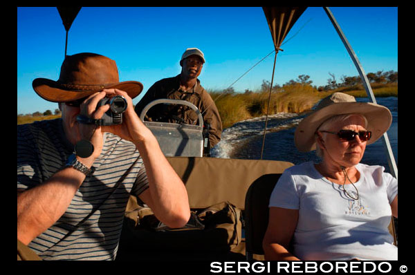Una parella de turistes gaudeix d'un safari en barca des del campament Eagle Island Camp d'Orient Express , als afores de la Reserva d'Animals de Moremi , a Botswana . Moremi Crossing es troba a la zona més meridional de Chief s Island , en una petita illa plena de palmeres i diferents arbres , anomenada Ntswi . Aquesta illa està envoltada per les riques planes al · luvials de Moremi . L'accés es realitza en avioneta , després d'un curt vol escènic des Maun d'uns 20 minuts de durada . Durant aquest vol panoràmic sobre el fascinant Delta de l' Okavango , podrà gaudir dels apassionants dibuixos que creen els serpentejants canals d'aigua i els contrastos de colors amb les zones de terra ferma que s'eleven sobre les aigües del Delta . A la zona nord del Delta les aigües Okavango flueixen de forma ràpida i la vista es veu limitada per les altes canyes i papirs que creixen en el límit dels canals. A la zona del sud del Delta , als voltants de Moremi CROSSING , es gaudeix d'àmplies vistes de les planes al · luvials de la reserva de Moremi 