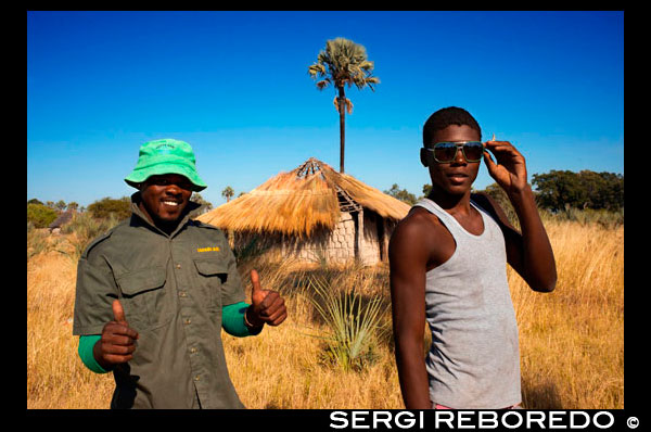 En la altea de la tribu Batawana es posible observar como han llegado los primeros efectos de la globalización, como lo muestra las gafas de sol y vestimenta de estas dos personas locales. En las inmediaciones del campamento Eagle Island Camp de Orient Express, en las afueras de la Reserva de Animales de Moremi, en Botswana hay un campamento donde residen un centenar de indígenas de la tribu Batawana. Es posible realizar excursiones en canoa para visitar su poblado. El Delta del Okavango es el delta interior más grande del mundo, un laberinto de lagunas, lagos y ocultos canales que cubre un área de 17 000 km cuadrados. Nace en Angola – numerosos afluentes se unen formando el Río Cubango, fluye a través de Namibia, convirtiéndose en el Río Kavango y entra finalmente en Botsuana, donde se convierte en el Okavango. Hace millones de años el Río  Okavango fluía hasta un gran lago interior llamado Makgadikgadi (actualmente conocido como Salares de Makgadikgadi - Makgadikgadi Pans). La actividad tectónica y fallas asociadas interrumpieron la corriente del río provocando un embolsamiento que ha dado lugar al Delta del Okavango. Esto ha generado un excepcional sistema de vías fluviales que sustenta una gran variedad de vida animal y vegetal en lo que de otra forma habría sido una árida sabana como la de Kalahari. Se calculan unos 200.000 grandes mamíferos en el Delta del Okavango y sus alrededores. En tierra firme y entre las islas que forma el delta, conviven leones, elefantes, hienas, perros salvajes, búfalos, hipopótamos y cocodrilos junto a una ingente variedad de antílopes y otros pequeños animales - facóqueros, mangostas, jinetas moteadas, monos, bebés arbustos y ardillas. Destaca la presencia en el Delta del Okavango del amenazado perro salvaje africano, constituyendo una de las manadas más densas de África. El delta también alberga más de 400 especies de aves, incluyendo el Águila Africana Pescadora. Muchos de estos animales habitan en el Delta pero la mayoría lo atraviesan, migrando en la época de lluvias estivales en busca de regeneradas tierras de pasto. Con el comienzo del invierno el campo se seca y los animales inician el camino de regreso hacia llanuras aluviales. Esto permite contemplar el impresionante espectáculo de ver avanzar unidos en una gran manada a los depredadores y sus presas. En ciertos lugares del Delta pueden verse las escenas más impactantes de depredadores del mundo.