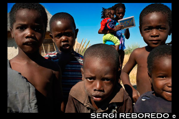 Un grupo de niños indígenas posan ante la cámara en el campamento Batawana. En las inmediaciones del campamento Eagle Island Camp de Orient Express, en las afueras de la Reserva de Animales de Moremi, en Botswana hay un campamento donde residen un centenar de indígenas de la tribu Batawana. Es posible realizar excursiones en canoa para visitar su poblado.  Los primeros habitantes de la actual Botswana fueron probablemente antepasados de los san (también conocidos como bosquimanos), cazadores y recolectores, que hoy habitan las estepas semiáridas de Botswana sudoccidental; y de los khoikhoi, provenientes del norte. Tribus de lengua bantú llegaron a la región en el primer siglo a.C. Los antepasados de los tswana, (hoy nación mayoritaria), se instalaron entre los siglos XI y XII en las llanuras del Río Vaal (hoy provincia sudafricana del Transvaal). Los tswanas se fundieron en ocho clanes poderosos. Las rivalidades entre clanes no permitieron a los tswana crear un reino como otras naciones en África del sur. La historia de Botswana –«la encrucijada fatal», ubicada en el corazón del sur de Africa–, es la historia del desierto de Kalahari, intermediario entre la poblada sabana del noreste y las despojadas estepas del suroeste. El tránsito precolonial posibilitó asentamientos de los británicos, holandeses y portugueses desde el siglo XVIII. Los británicos intentaron unir el continente de norte a sur (desde Sudáfrica a Egipto), tomando la «ruta de los misioneros». Los portugueses quisieron unir las colonias de Angola y Mozambique. La región fue una verdadera encrucijada entre los intereses estratégicos coloniales, y entre éstos y las tribus tswanas que habitaban esas zonas desde el siglo XVII. En 1840, se asentaron en el este de Botswana (región de Transvaal) los colonos holandeses boers (conocidos también como afrikaaners), que huían de los ingleses establecidos en Ciudad del Cabo (Cape Town). Los boers (agricultores) disputaron las escasas tierras fértiles con los tswanas, provocando además conflictos entre éstos y los zulúes a los que los colonos expulsaron del sur de África. En 1895 tres reyes tribales Tswana fueron a Londres buscando apoyo contra los boers y contra la expansión alemana por el sudoeste africano. Botswana se transformó desde allí en un protectorado británico, conocido como Bechuanaland. Los reyes debieron conceder, a cambio de protección, que la Compañía Británica de Sudáfrica (forma de privatización y expansión inglesa), construyera una vía férrea entre sus tierras y Zimbabwe (Rhodesia). La tutela inglesa impidió la absorción política por parte de Sudáfrica, pero facilitó la dominación económica de los boers. Pese a su vasta región semidesértica, Botswana se convirtió en uno de los principales exportadores de ganado y carne de África austral. A comienzos del siglo XX, el 97% de la población vivía en el campo y cada familia poseía al menos un par de vacas; los más ricos tenían bueyes para arar la tierra. En 1966, cuando Botswana logró su independencia, la población urbana llegó al 15% y casi el 40% de los habitantes rurales no poseía ganado. Debido a la concentración económica los afrikaaners dominaron la agricultura y controlaron el 60% de las exportaciones de carne. La lucha independentista se confundió, en varios momentos, con un asunto matrimonial. Seretse Khama, uno de los herederos más influyentes de la etnia bamangwato, estudió derecho en Inglaterra y se casó con Ruth Williams, una oficinista europea. La boda escandalizó a los ingleses y a los afrikaaners, que impidieron a Seretse volver a su tierra natal. Seretse resistió las presiones, incluso ofertas de dinero de los ingleses y, con el apoyo masivo de su pueblo, mantuvo el liderazgo de la tribu más importante del país. No volvió hasta 1956. Nueve años después, en elecciones generales, su partido, el Partido Democrático de Botswana (BDP), obtuvo 80% de los votos. Con la independencia, Seretse fue elegido primer presidente del país. En 1967, fue designado caballero del Imperio Británico. El BDP, llevó a cabo una política conciliadora en relación a los habitantes de origen europeo, que manejaban el 80% de la economía. Botswana formó parte de los países de la Línea del Frente que luchaban contra el apartheid (ver Sudáfrica) e integró la SADCC (ver Organizaciones Internacionales), que buscaba romper la dependencia económica de los nueve países negros del África austral con respecto a Sudáfrica. En 1980 Seretse murió de cáncer y fue sucedido por el vicepresidente Quett Masire (doctorado en economía en Oxford), quien sufrió fuertes presiones de grupos de orientación socialista revolucionaria, en lo referente a limitar la concentración de tierras fértiles en manos de europeos y a aumentar el área destinada a cooperativas. Los campesinos acusaron a los grandes hacendados de criar demasiado ganado en tierras pobres, las que quedarían inútiles a corto plazo. Surgió, además, un movimiento a favor de nacionalizar los yacimientos de diamantes, cobre y níquel, explotados por empresas sudafricanas.