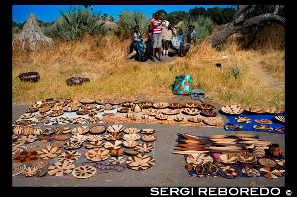 Improvisado mercadillo de artesanía a la llegada de los turistas en el campamento Batawana. En las inmediaciones del campamento Eagle Island Camp de Orient Express, en las afueras de la Reserva de Animales de Moremi, en Botswana hay un campamento donde residen un centenar de indígenas de la tribu Batawana. Es posible realizar excursiones en canoa para visitar su poblado.  La Artesanía de la terracota en el Distrito de Kgatleng de Botsuana fue declarada Patrimonio cultural inmaterial de la Humanidad en 2012 por la UNESCO.1 Se trata de la artesanía creada por las mujeres de la comunidad bakgatla ba kgafela del Distrito de Kgatleng, en el sudeste del país. Se utiliza tierra arcillosa, arenisca erosionada, óxido de hierro, boñiga de vaga, agua, hierba y madera para fabricar recipientes en los que se plasman motivos de rituales y creencias ancestrales de la comunidad. La recolección de la tierra se hace a través de la meditación de la maestra artesana. Una vez recolectadas la arcilla y la arenisca, se machacan y se criban. Tras ello se forma la pasta para modelar. Tras decorarse, se cuecen en un horno de pozo. La tradición se va trasmitiendo de generación en generación pero actualmente este arte corre peligro de desaparición debido a la disminución del número de maestras artesanas, los bajos precios de los productos acabados y el uso, cada vez más, de recipientes de producción de masa. Es por ello que la UNESCO lo incluyó en la Lista del Patrimonio Cultural Inmaterial que requiere medidas urgentes de salvaguardia.