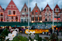 Bruges. La Plaça Markt i Burg estan ubicades al centre del nucli antic i són dos bons llocs per començar la visita. El Markt és la plaça principal de Bruges. Aquesta zona està envoltada de acolorides botigues i restaurants. La Grote Markt o Plaça del Mercat a Bruges. Aquesta plaça va ser utilitzada com a mercat, ja 958, i un mercat setmanal es va celebrar aquí des 985 a agost de 1983 - gairebé un miler d'anys! Avui en dia la gran plaça està envoltada per bancs (amb caixers automàtics), una oficina de correus, i moltes cases gremials convertides en restaurants a l'aire lliure. El Mercat s'omple de vianants i ciclistes, i és un bon lloc per començar o finalitzar una visita a peu de la ciutat. El Campanar s'alça a l'extrem sud de la Plaça del Mercat a Bruges. 