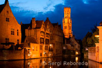 Brujas por la noche con la torre del campanario en el fondo, el paisaje más típico de Brujas. Por la noche es recomendable dar una paseo para observar las vistas sobre Brujas en el canal Dijver y la torre del campanario ilumninados. 