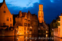 Brujas por la noche con la torre del campanario en el fondo, el paisaje más típico de Brujas. Por la noche es recomendable dar una paseo para observar las vistas sobre Brujas en el canal Dijver y la torre del campanario ilumninados. 