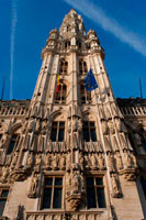Hôtel de Ville. L'edifici de l'ajuntament, que ocupa la façana sud-oest, és l'únic edifici medieval que queda avui en dia en peu i va ser construït entre 1402 i 1455 probablement per Jean Bornoy. La seva torre, asimètrica pel que fa a l'edifici, de 96 metres d'altura, és d'estil gòtic i va ser dissenyada per Jean van Ruysbroeck en 1449. Una llegenda urbana compte que l'arquitecte, en comprovar el suposat error que la torre no quedés situada al centre, va pujar a aquesta i es va llançar al buit, encara que en veritat ambdues parts no van ser construïdes a la vegada. A sobre de la torre es troba una alta estàtua de bronze de 5 metres de l'arcàngel Miquel, patró de Brussel · les, matant a un drac o dimoni. La part esquerra de l'ajuntament consta de dotze arcs, inclòs el campanar, que representen l'alquímia humida en dotze etapes. En canvi, el costat dret té únicament amb set arcs, comptant el campanar, que simbolitzen la nova alquímia seca, en set etapes. La façana està decorada amb nombroses estàtues que representen els nobles, els sants i figures al · legòriques.