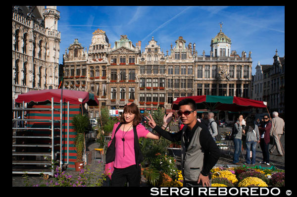 Dos xinesos es fotografien a La Grand Place. Coneguda per la seva bella arquitectura, aquesta és la principal plaça de Brussel · les i està catalogada com una de les millors ornamentades del món. Va ser inscrita a la llista del patrimoni mundial de la UNESCO el 1998, i en ella se situen edificis de vital importància com l'ajuntament gòtic del segle XV i altres no menys pintoresques que daten del segle XVII. Lamentablement, el 1965, durant la Guerra de la Lliga d'Augsburg, la major part dels edificis, en ser de fusta, van quedar reduïts a cendra, resistint únicament alguns que estaven construïts en pedra. Llavors els mercaders de la zona es van reunir i van tornar a edificar, aquesta vegada en pedra, el colossal conjunt arquitectònic que podem veure avui en dia. A l'agost, cada dos anys, els horticultors de Gant col · loquen una catifa de flors que ocupa 25 X 75 metres al mig de la plaça. XINESOS AMB CÀMERA