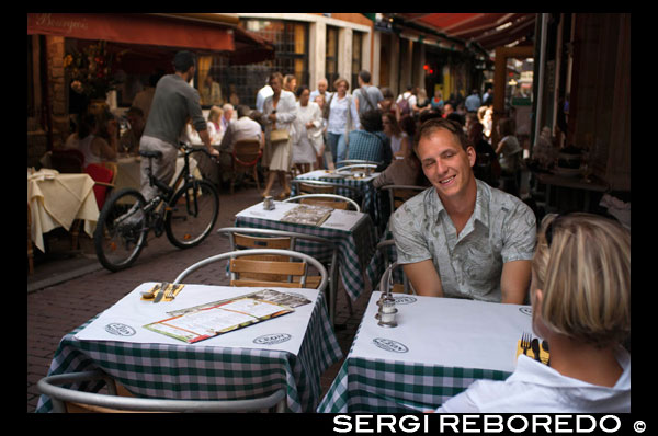 Una pareja en uno de los muchos restaurantes del barrio de Ilôt Sacré y Jardin Botanique. El origen de Ilôt Sacré se sitúa a finales de los años 50, cuando Bruselas estaba inmersa en la preparación de la Exposición Universal de 1958. Con el fin de mejorar el tráfico rodado y facilitar el acceso de turistas, se acordó ampliar y modificar el centro de la ciudad. Edificios con siglos de historia ubicados en las calles Rue des Bouchers y Rue des Dominicains fueron derribados para dar paso a calles y avenidas más anchas. A principios de los 60 los propietarios se unieron para proteger los edificios históricos que quedaban en pie creando islotes (ilôts en francés) que conservaran su patrimonio. ROMANTICISMO EN BRUSELAS