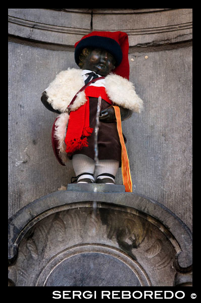 Manneken Pis. Rue de l’Étuve, 46 esquina Rue du Chêne. <M> Bourse. Esta estatua de bronce de apenas 30 centímetros de un niño desnudo haciendo pis en una fuente es el símbolo por excelencia de la ciudad. Esculpida por Jérôme Duquesnoy en 1619, sufrió varios intentos de saqueo en siglos posteriores hasta que por fin consiguieron robarla en 1960, aunque fue recuperada poseriormente. Para preservarla,  actualmente se exhibe una copia de bronce, y el original descansa en el Musée de la Ville de Bruselas. Varias leyendas sitúan su procedencia, unos dicen que el hijo de un duque se puso a orinar en medio de una batalla que acabaron ganando y la estatua consagra ese coraje militar, otros dicen que un niño llamado Juliaanske vio como colocaban dinamita en las murallas y, antes de que la mecha detonara la carga, consiguió orinar encima deteniendo de esta manera la explosión y salvando la ciudad de una conquista. Fuere como fuere hoy en día es un mito y cuenta con más de 800 trajes diferentes pertenecientes a todo tipo de culturas y naciones. Entre éstos figuran, por ejemplo, trajes típicos de varias comunidades autónomas españolas, de torero, del cid campeador, del barça y del Madrid, de castellers de Vilafranca e incluso de la cofradía de la Hermandad de Cruzados de la Fe. VESTIDO CON EL TRAJE DE LA DIADA DE CATALUNYA.