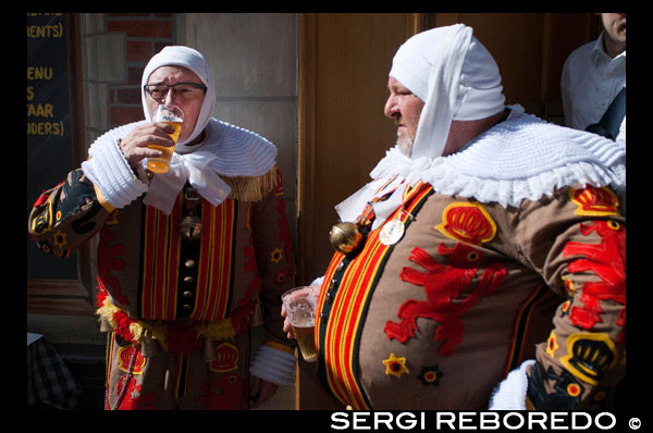 Two participants Binche Belgian festival drinking beer in their traditional costumes: Eastern princes, sailors and Harlequins also walk the streets of Brussels. An amazing procession through the cobbled streets of the city to the beat of drums and artists with their wax masks and ostrich feathers. Quite an experience. HUGE beer belly.