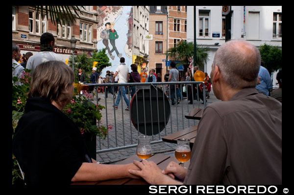 Una pareja tomando una cerveza y admirando una de las muchas pintadas de comics que se encuentran repartidas por la ciudad. Una treintena de paredes de la ciudad están pintadas con viñetas de algunos de los más famosos personajes de la historia del cómic. Los Pitufos, Espirú o Lucky Luke tienen algo en común con Tintín y Astérix: son belgas. Bruselas no actúa sólo como capital de la Unión Europea, es también el centro del cómic del antiguo continente. Está tan arraigado en esta ciudad como los gofres, el chocolate o la cerveza. UNA PAREJA TOMANDO CERVEZA EN UNA PLAZA.